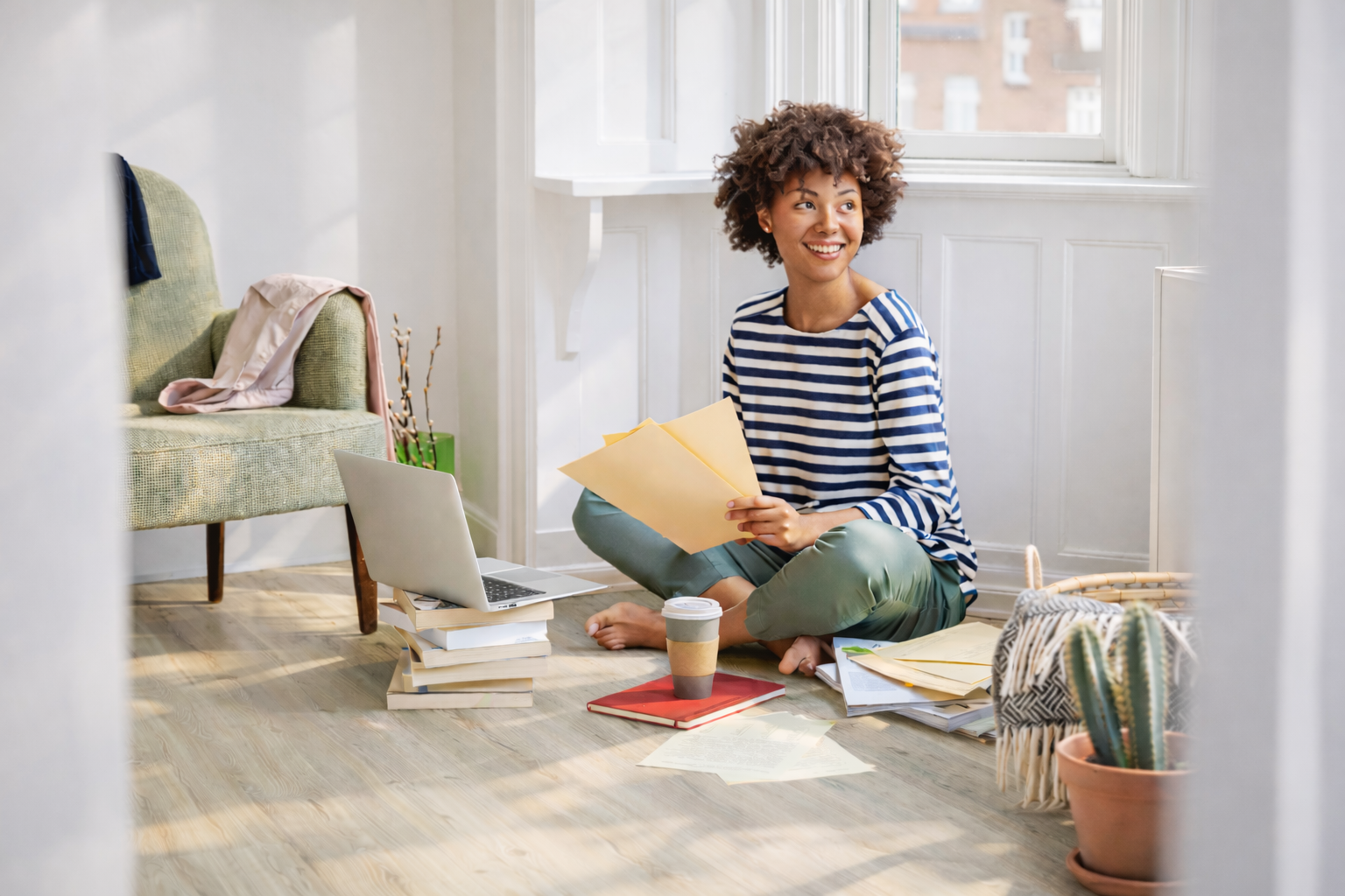 MyVinyl_Imagebild_BlogundRatgeber Frau sitzt auf dem Boden mit Laptop, Kaffee und Papieren, umgeben von Büchern in einem hellen Raum