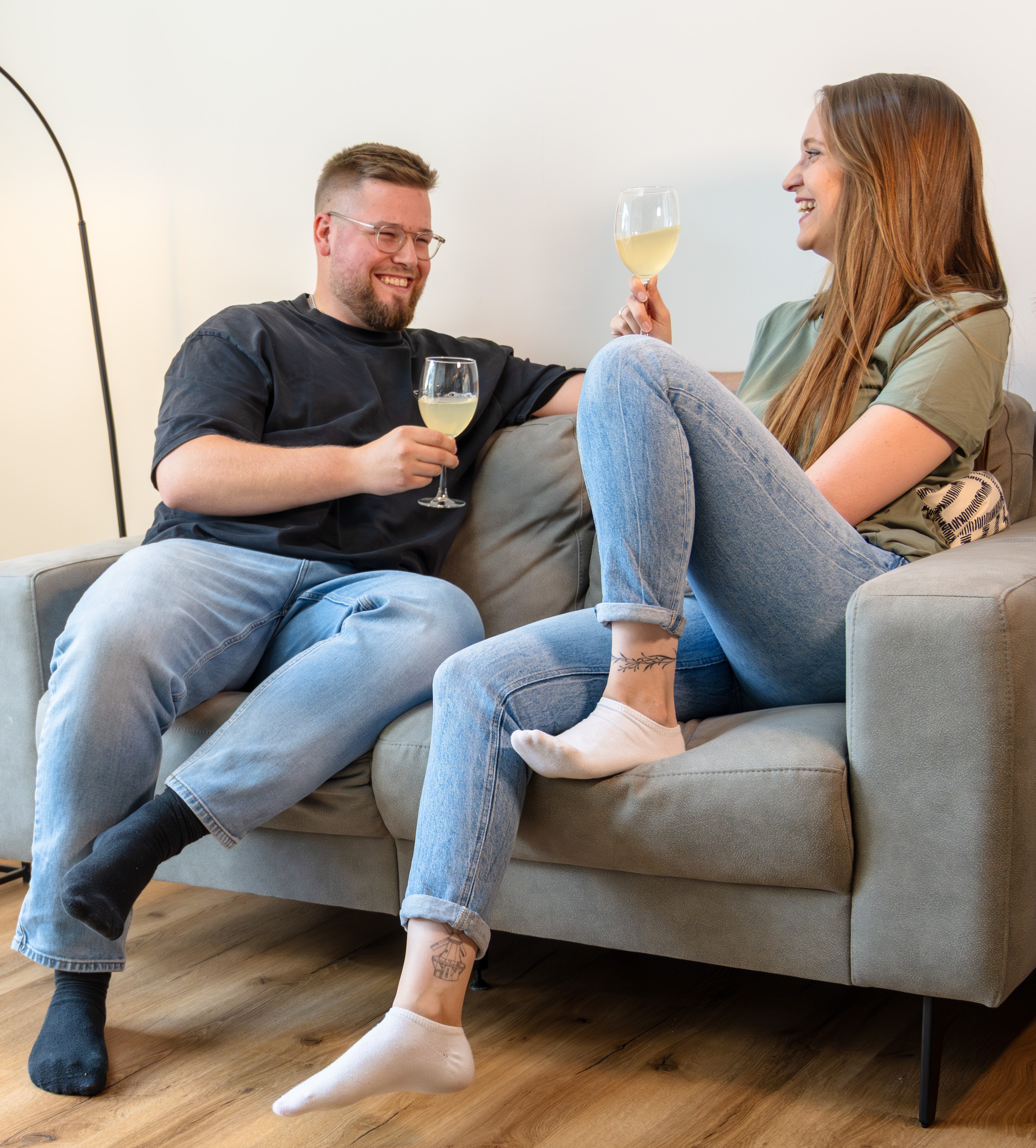 Junge Frau in Latzhose kniet auf dem Boden und hält lächelnd ein helles Laminatbrett in einem renovierungsbedürftigen Raum