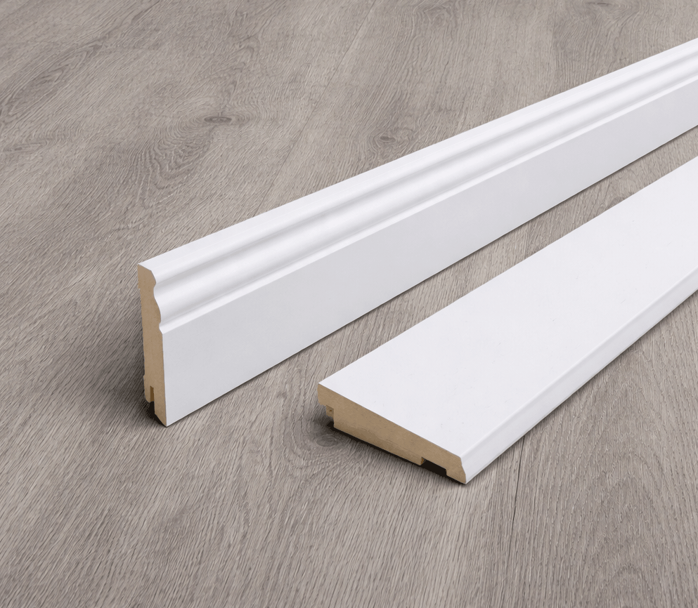 Junge Frau in Latzhose kniet auf dem Boden und hält lächelnd ein helles Laminatbrett in einem renovierungsbedürftigen Raum